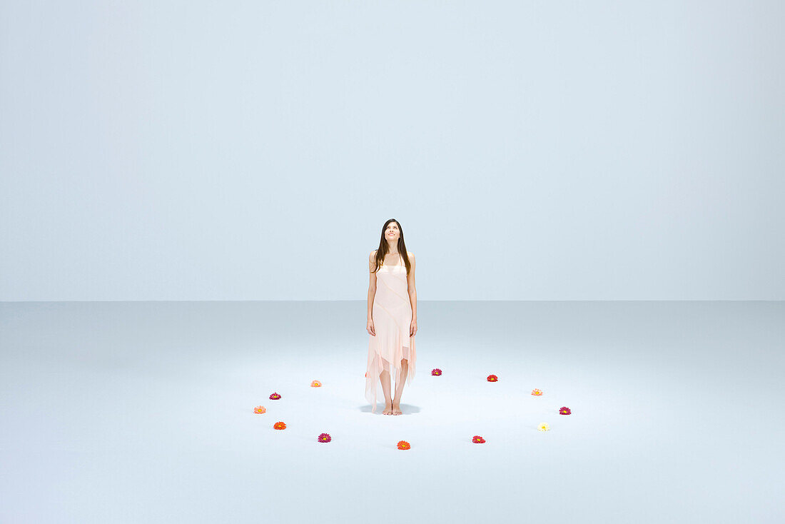 Young woman standing within circle of flowers, looking up