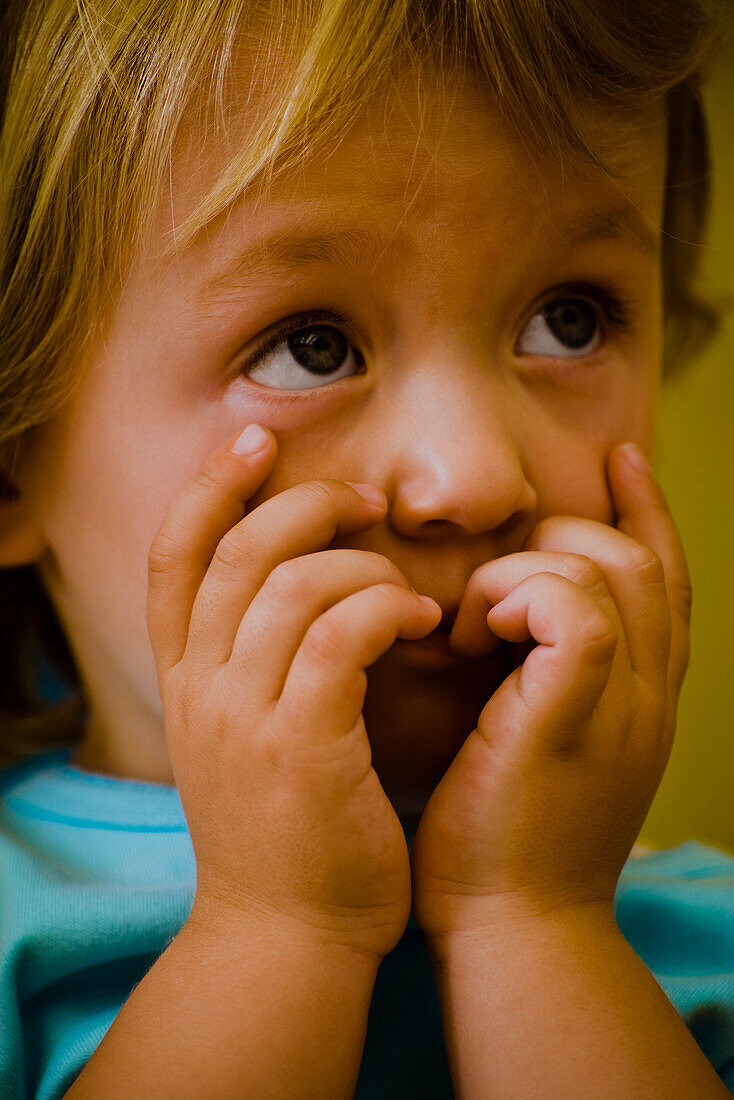 Toddler girl covering mouth with hands, shyly looking up