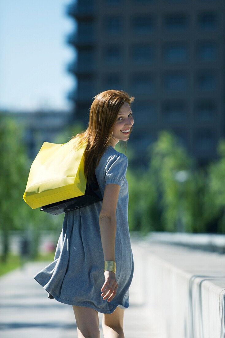 Young woman carrying shopping bags, smiling over shoulder at camera