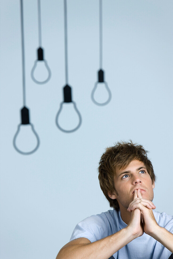 Young man looking up in thought, hands clasped in front of mouth