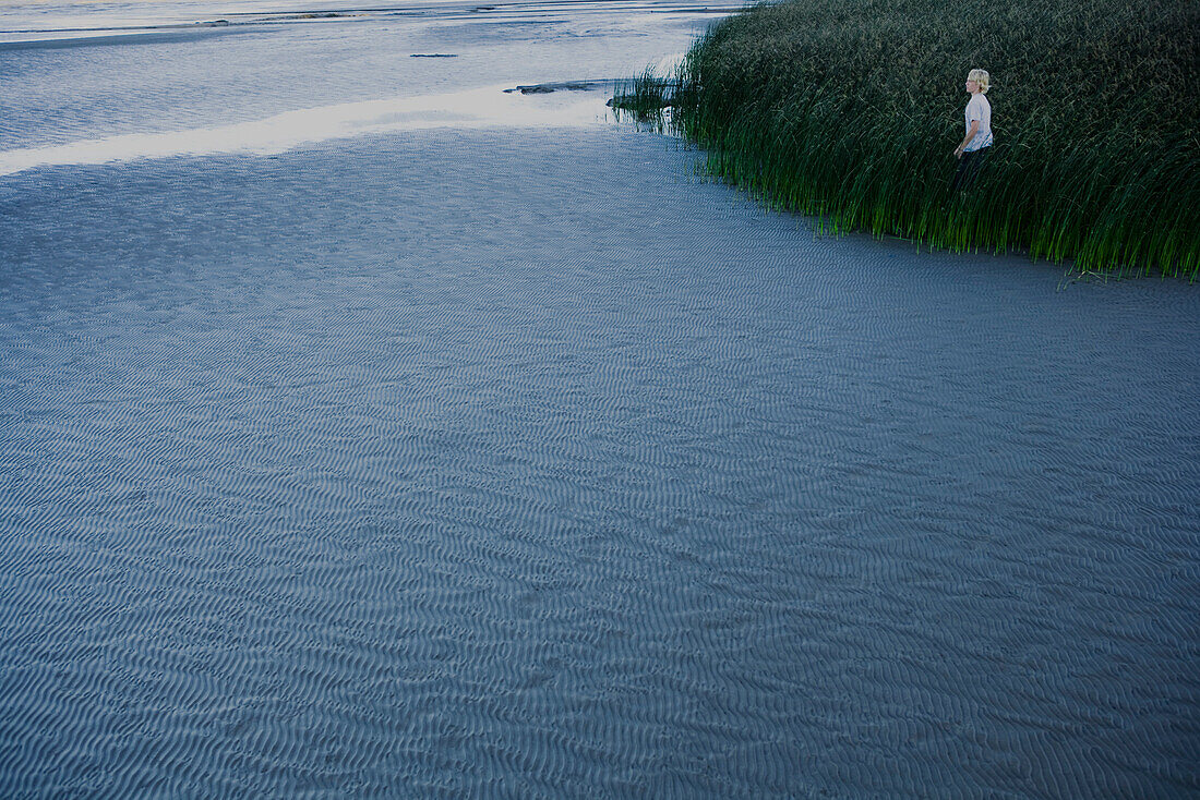Young man standing in tall grass along coast at low tide