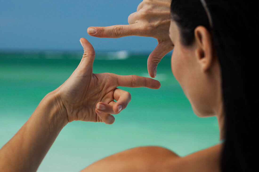 Woman at beach, looking at sea through finger frame