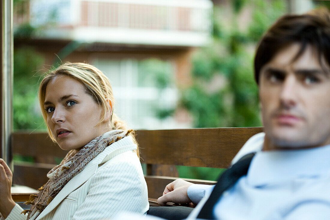Couple sitting outdoors, woman looking away in distraction