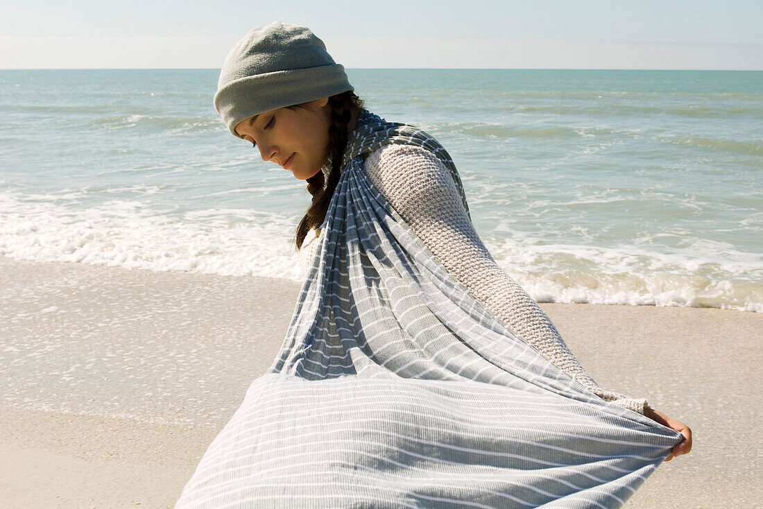 Teenage girl walking on beach, holding out scarf in breeze