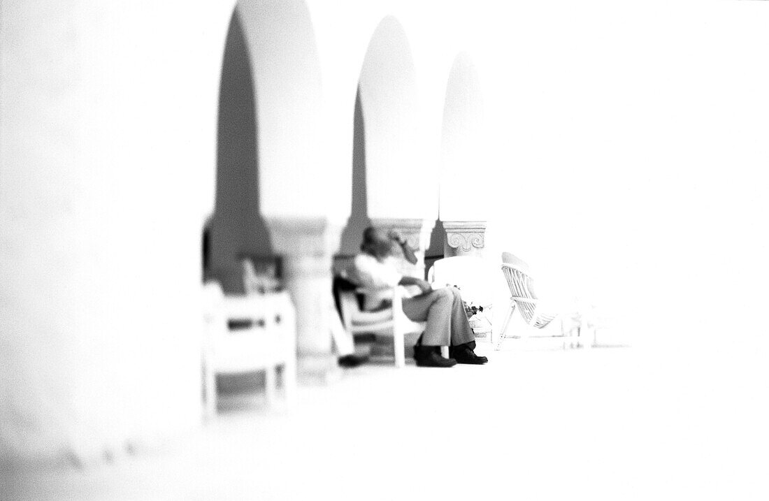 People sitting in chairs under arches, b&w