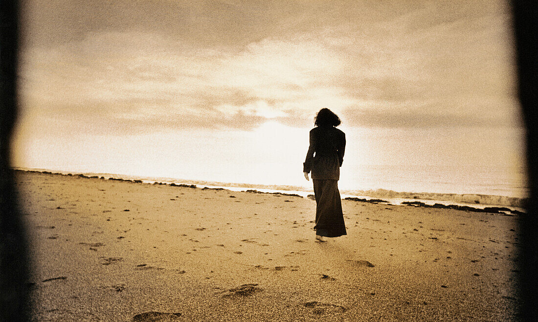 Woman walking on beach, b&w, toned