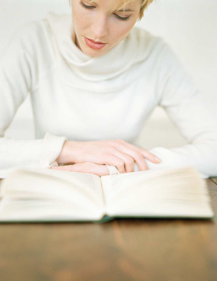 Frau sitzt am Tisch und liest ein Buch