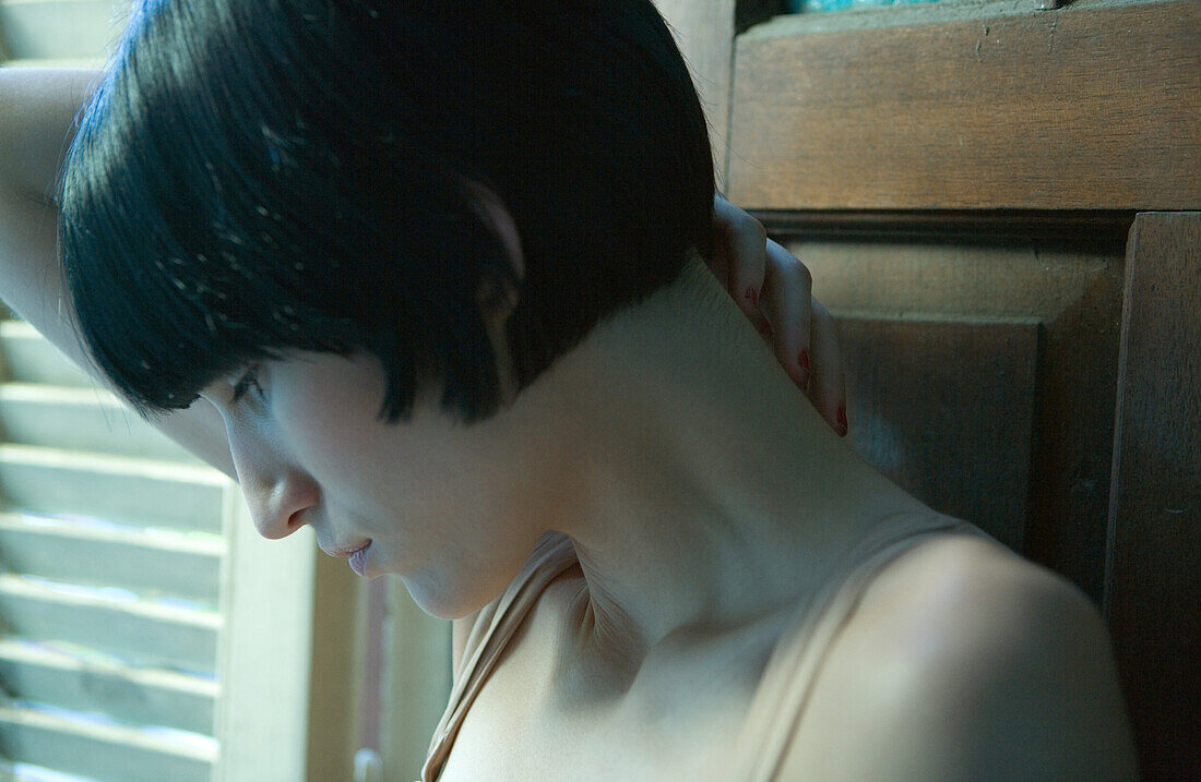 Close-up of woman looking down, hand on back of neck, head and shoulders