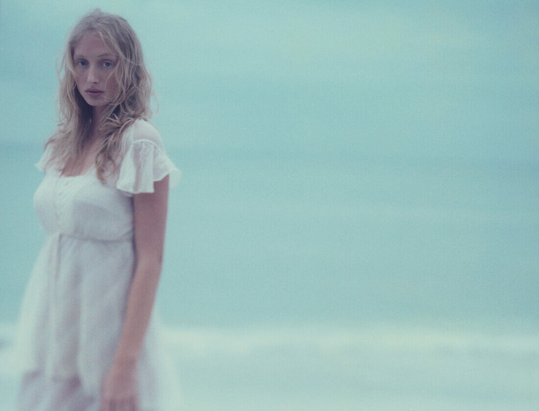 Young female in dress looking at camera, ocean in background