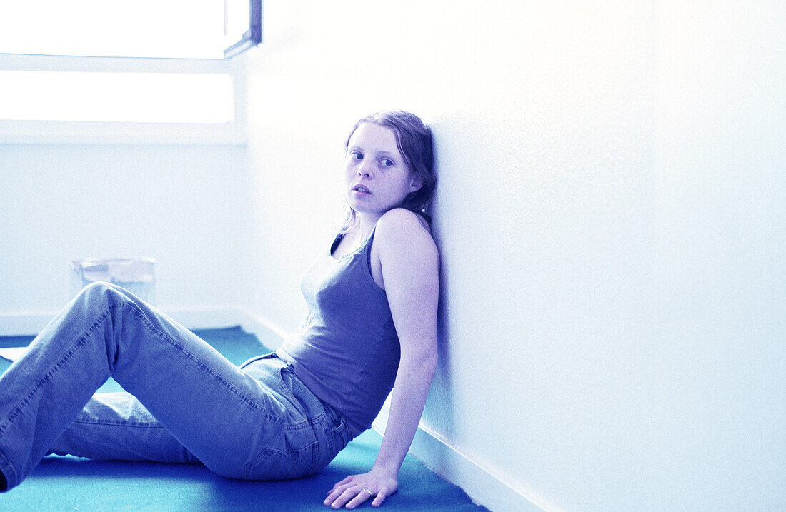 Young woman sitting on floor, leaning against wall