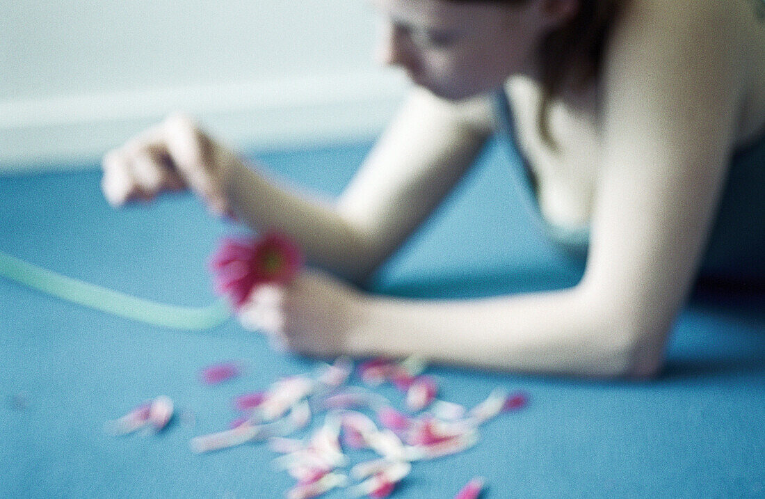 Young woman pulling petals off flower, blurred