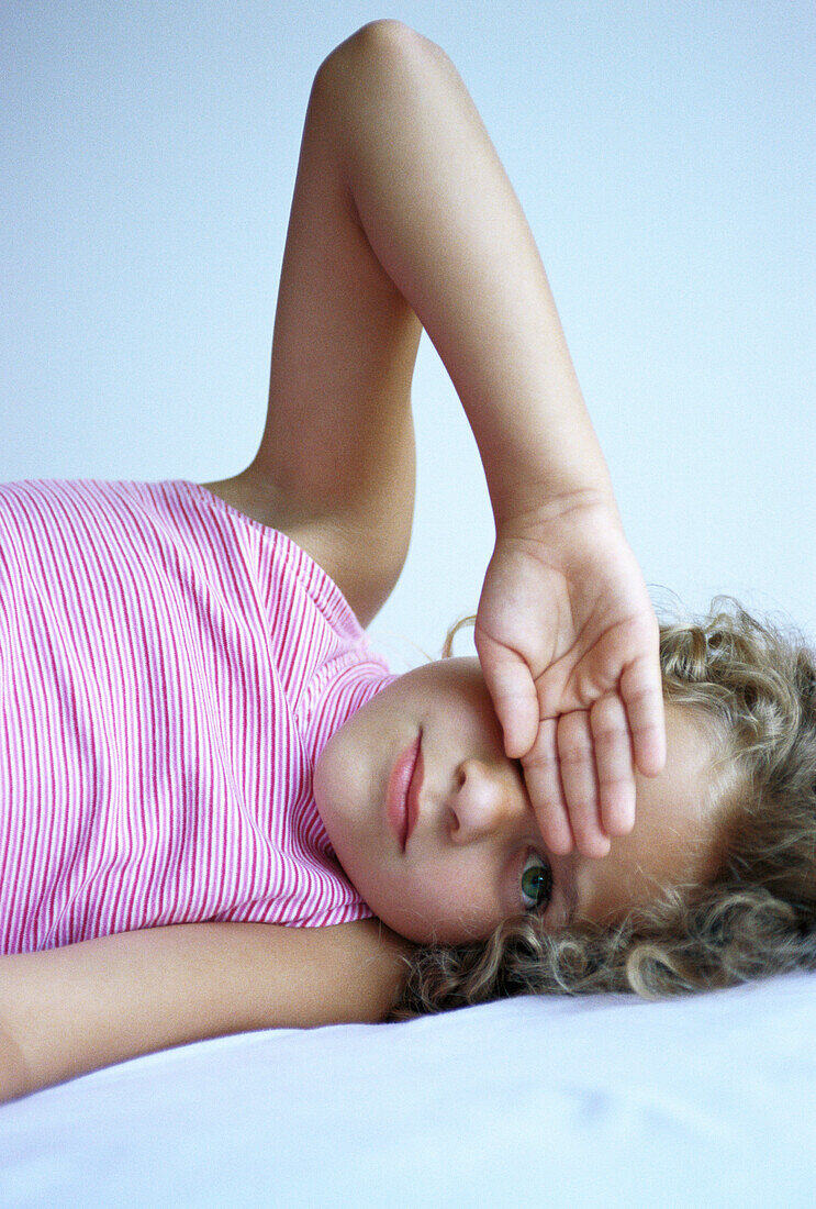 Girl lying in bed with hand over eye