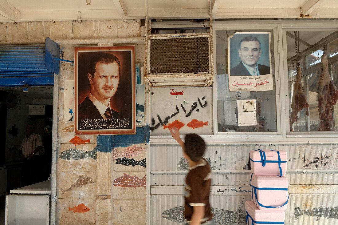 Syria, Tartus, passer-by in front of a fish shop, Bachar al Assad president on posters
