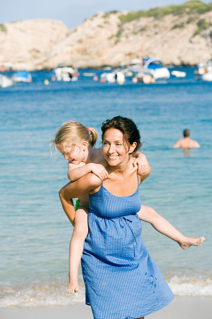 Woman giving piggyback to girl at seaside