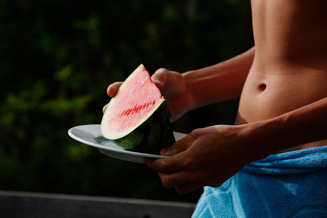 Teen boy holding a slice of watermelon on a plate