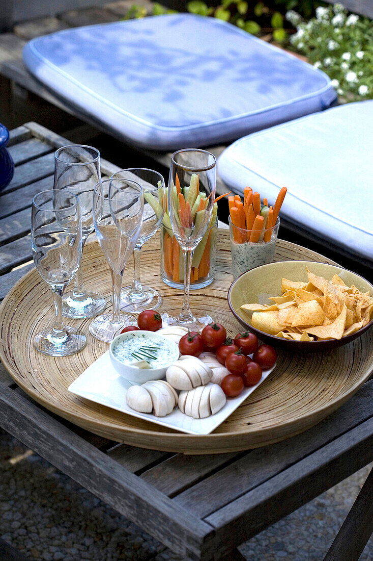 Chips, vegetables and glasses on a table on terrace