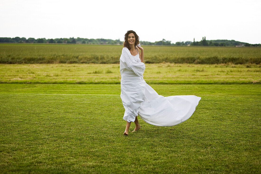 Young woman in a field, white sheet on her body, oudoors