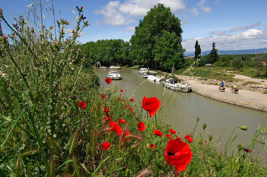 Boats on the canal du Midi with two cyclists cycling past, Beziers, Midi, France
