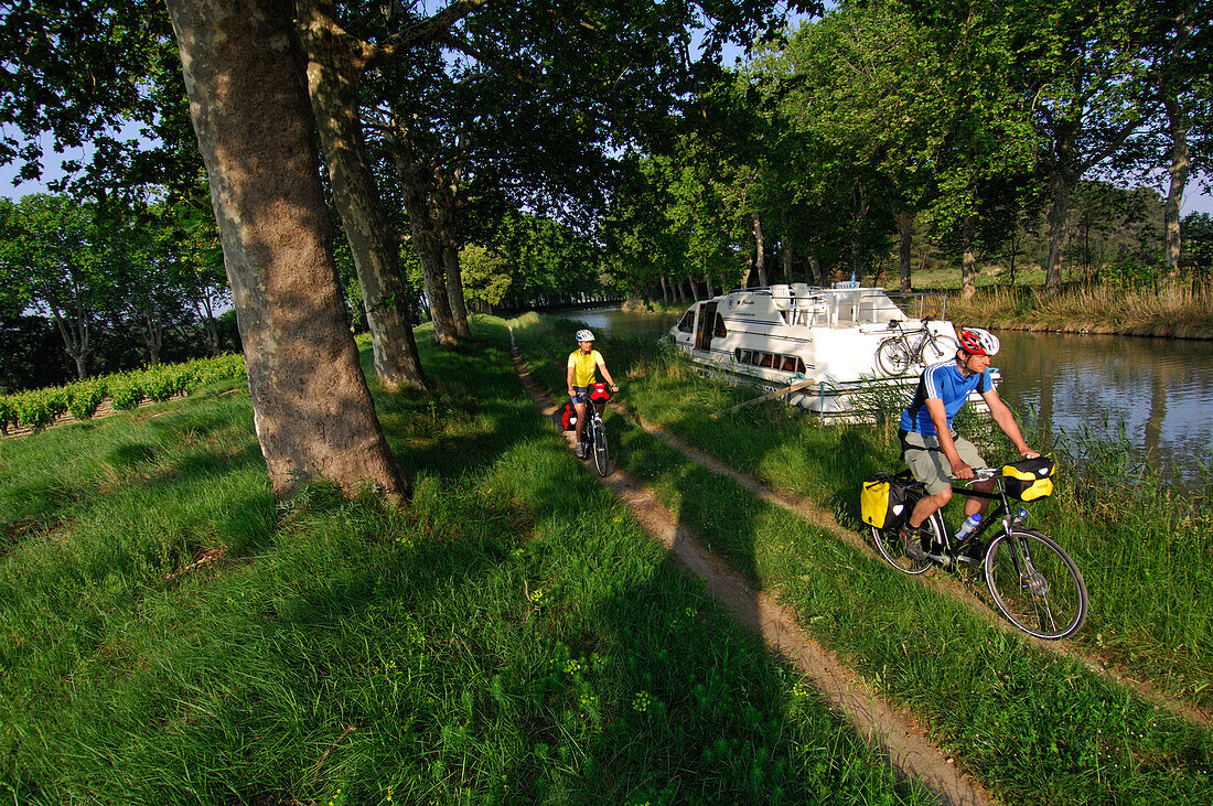 Cyclists cycling past a boat, Canal du Midi, Midi, France