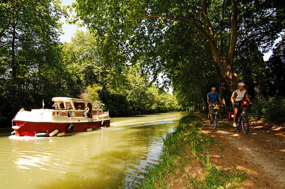 Two cyclists cycling along a path next to the Canal du Midi, Midi, France