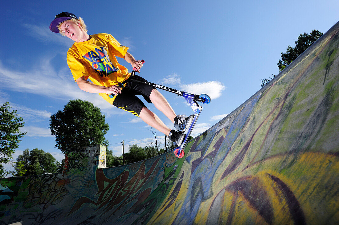 Junger Mann im Sprung mit einem Tretroller, Skatepark, München, Oberbayern, Bayern, Deutschland