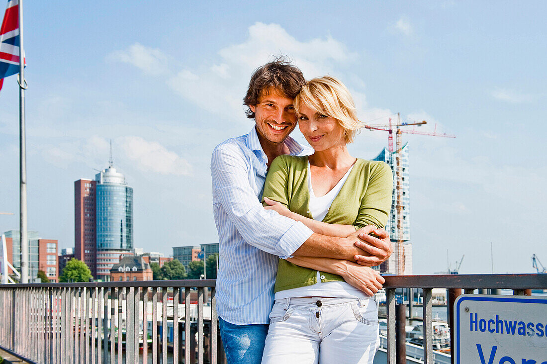 Couple smiling at camera, Elbe Philharmonic Hall construction site in background, HafenCity, Hamburg, Germany