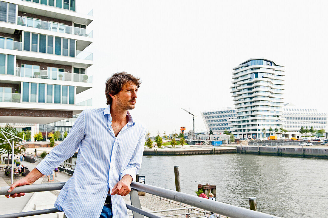 Mann mittleren Alters lehnt an einem Geländer, Marco-Polo-Tower im Hintergrund, HafenCity, Hamburg, Deutschland