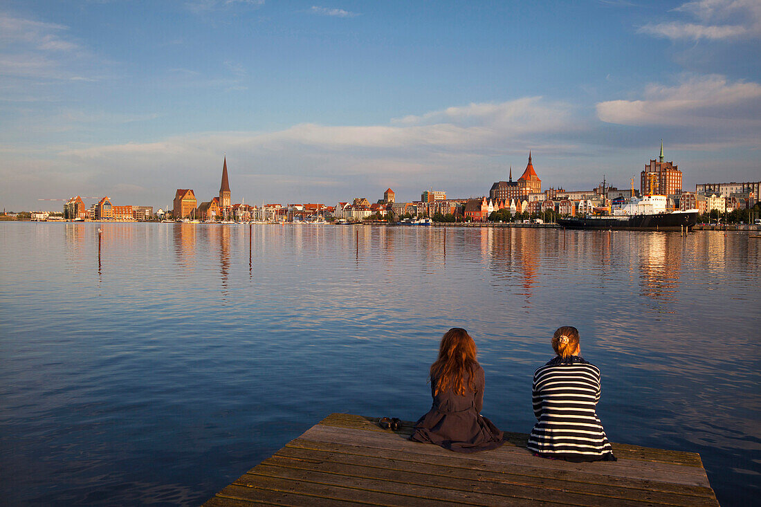 Zwei Frauen sitzen auf einem Bootssteg, Blick über die Warnow zur Altstadt mit Marienkirche, Rostock, Ostsee, Mecklenburg-Vorpommern, Deutschland, Europa