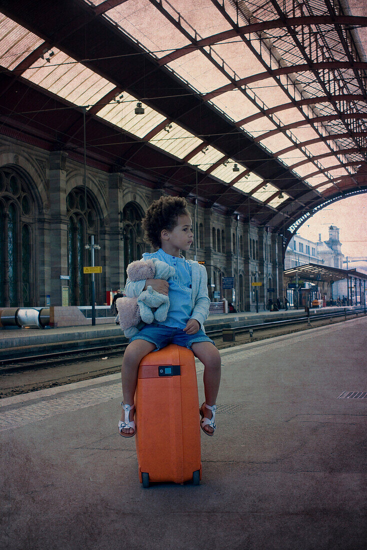 Little girl sitting on suitcase waiting in train station