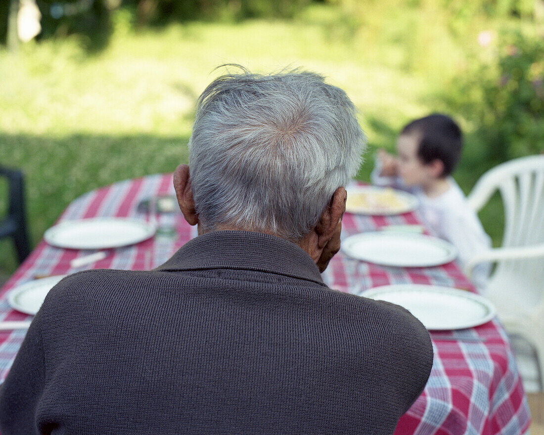 Senior man sitting at table outdoors, contemplating grandchild