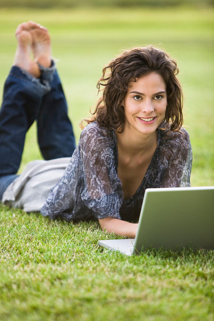 Young woman lying in grass, using laptop computer
