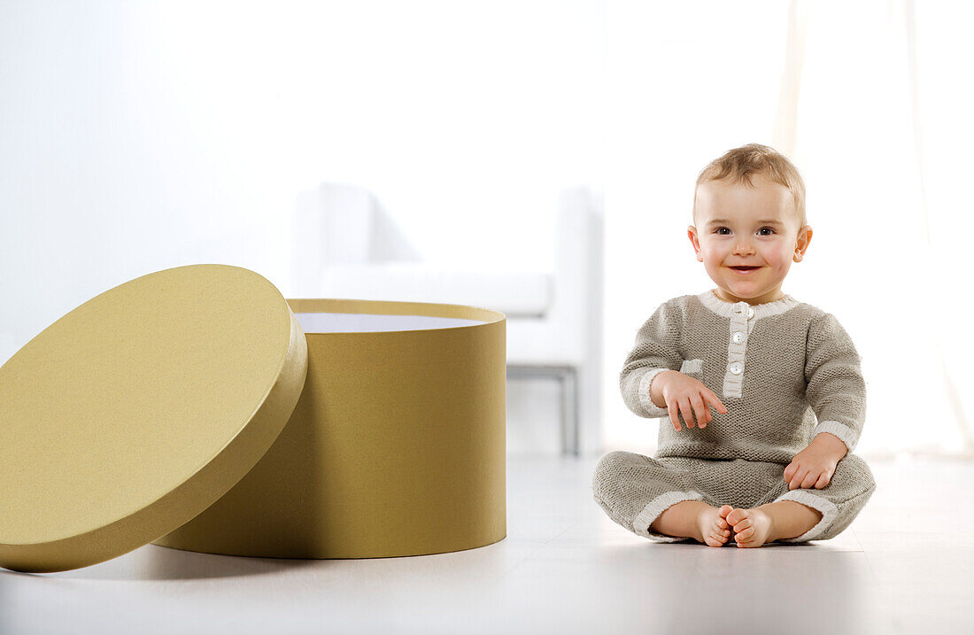 Smiling baby boy sitting on floor, next to box
