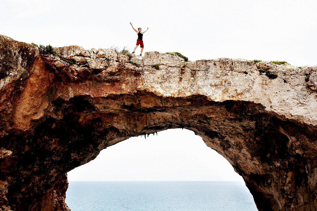 Celebrating Female Rock Climber Standing on Top of Arched Rock Formation, Cala Barques, Mallorca, Spain