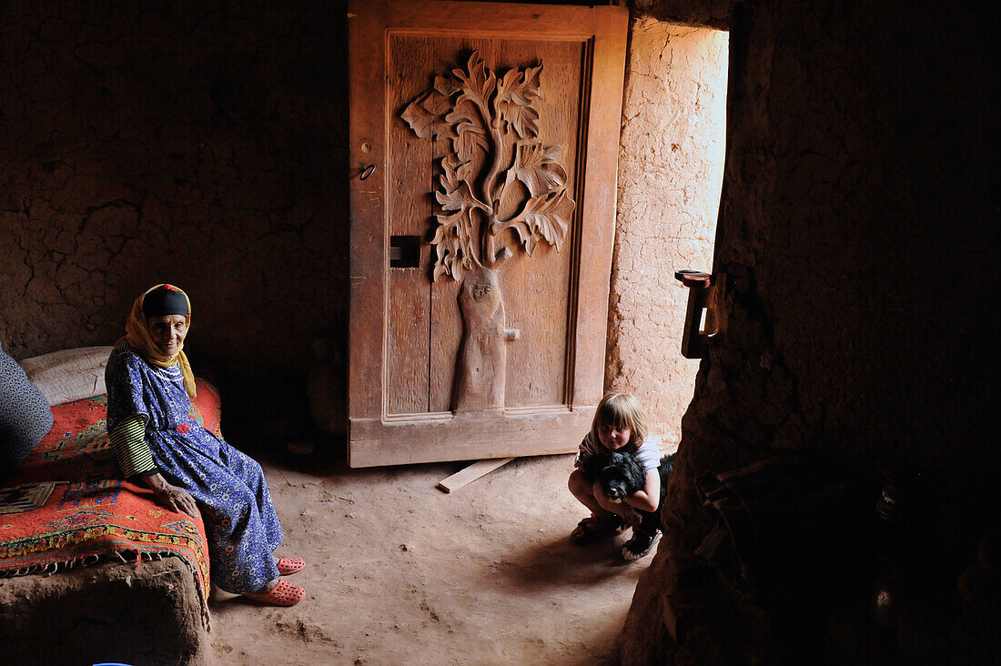 Alte Berberfrau und kleines europäisches Mädchen in Lehmhaus mit verzierter Tür, Kasbah in Ait Benhaddou südlich vom Hohen Atlas, Marokko, Afrika