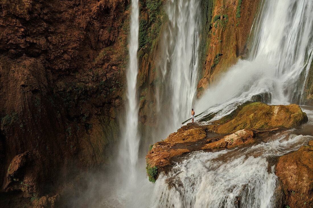 Mann steht auf Klippe im Wasserfall bei Ouzoud, Hoher Atlas, Marokko, Afrika