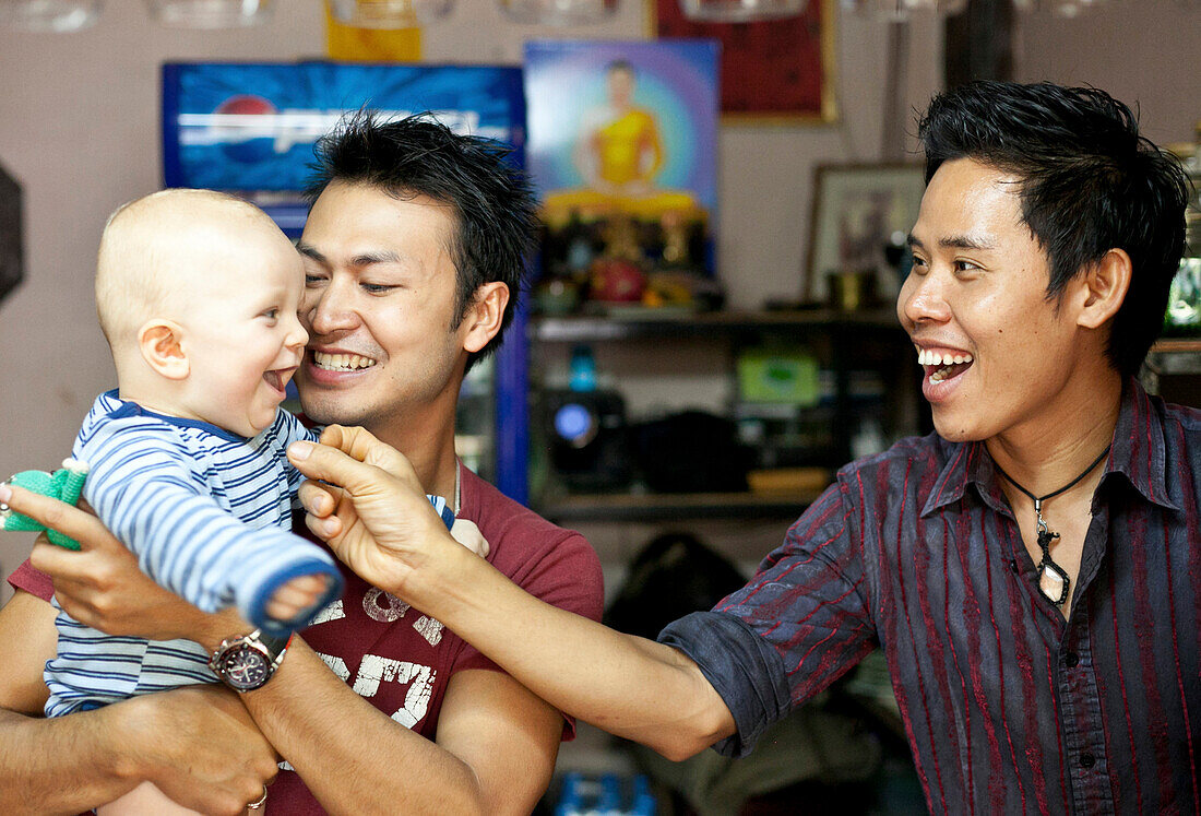 Zwei junge Thai Männer spielen mit deutschem Baby in einer Bar, Pai, Thailand, Asien