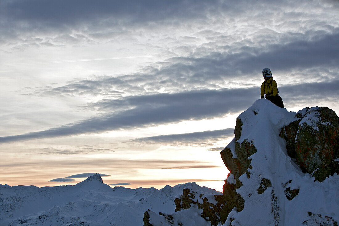 Snowboarder steht auf einem Berggipfel in der Abenddämmerung, Chandolin, Anniviers, Wallis, Schweiz