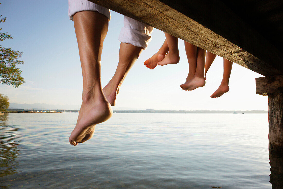 Father and three children sitting on a jetty, close-up feet, Lake Starnberg, Bavaria, Germany