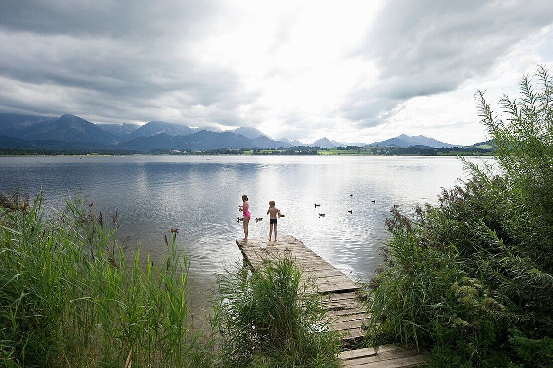 Two children on a jetty at lake Hopfensee, Fuessen, Allgaeu, Bavaria, Germany