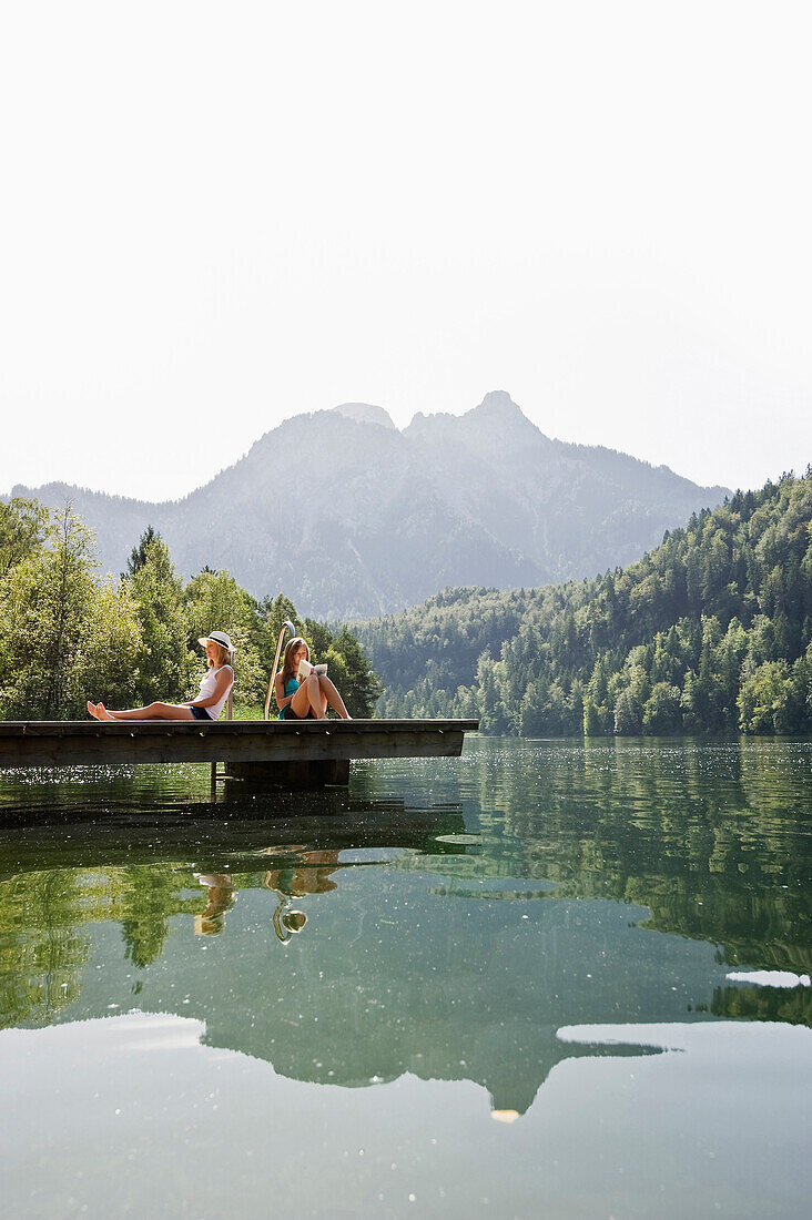 Two teenage girls sitting on a jetta at lake Schwansee, Schwangau, Allgaeu, Bavaria, Germany