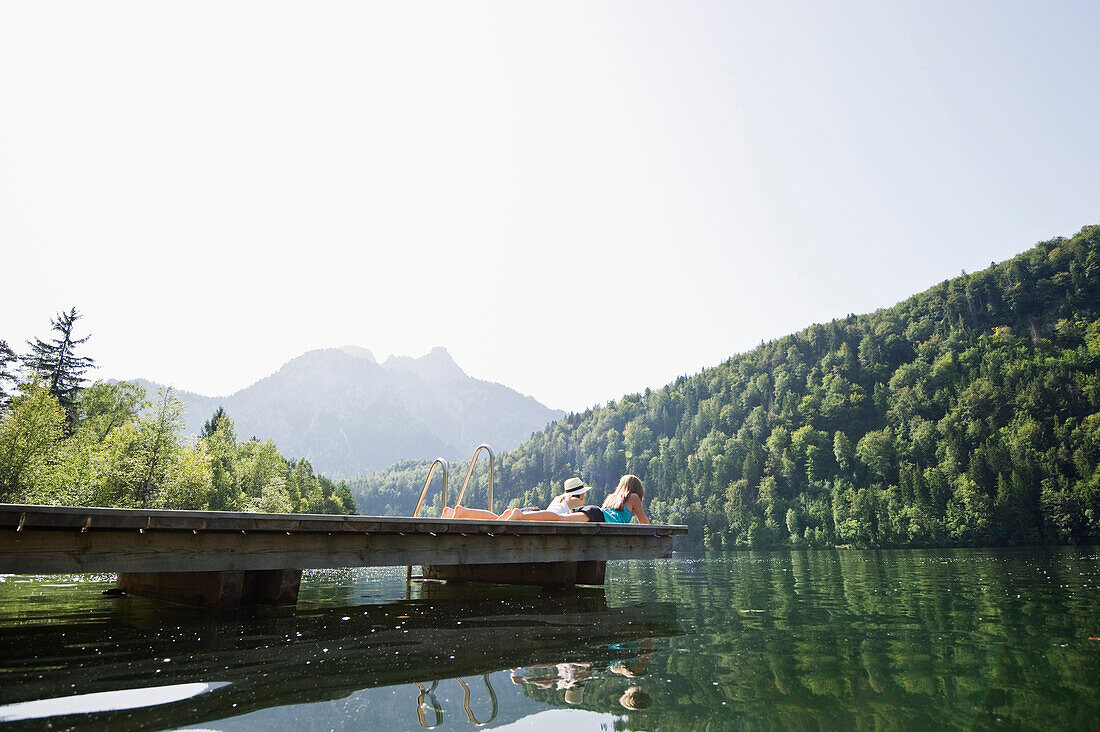 Two teenage girls lying on a jetty at lake Schwansee, Schwangau, Allgaeu, Bavaria, Germany
