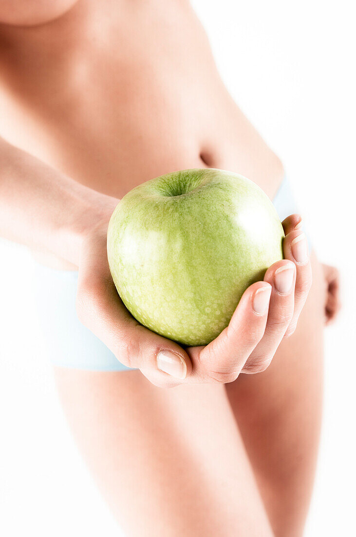 Naked woman in panties, holding a green apple, close up (studio)