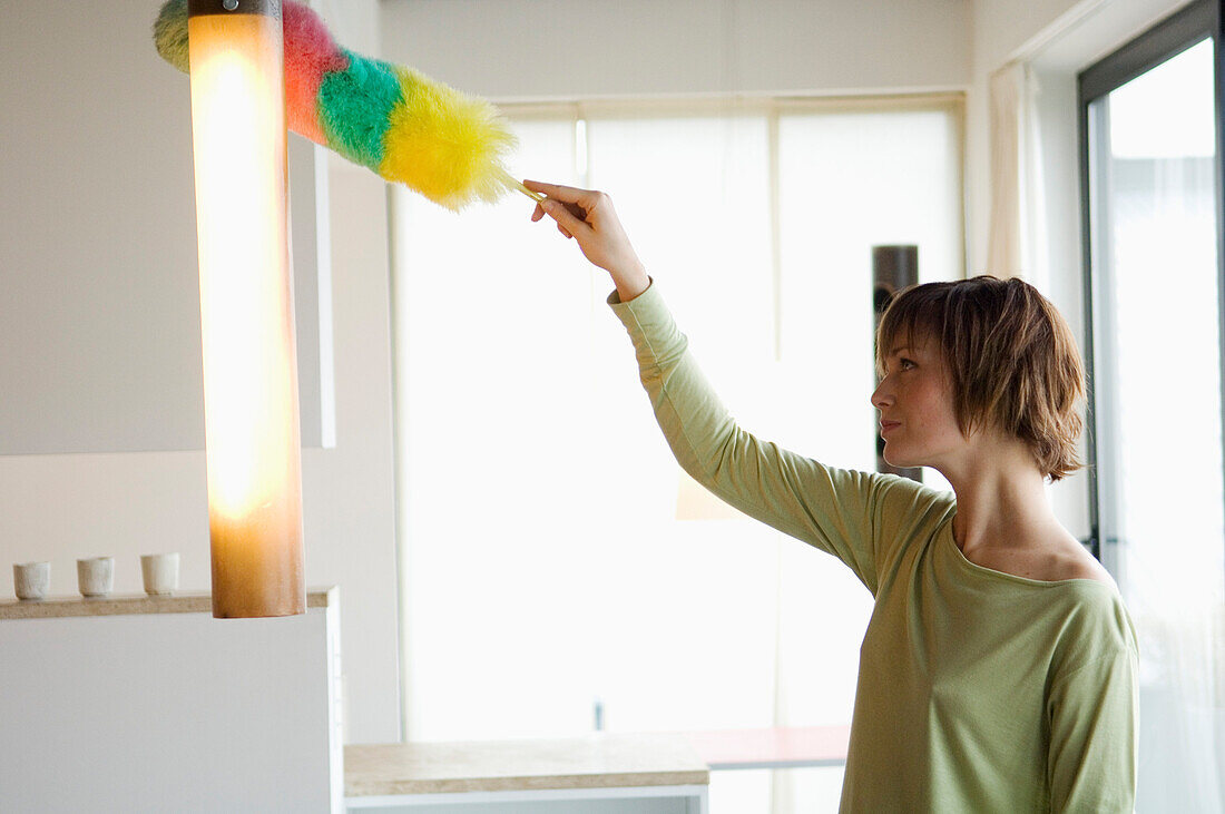 Woman dusting a lamp with a feather duster