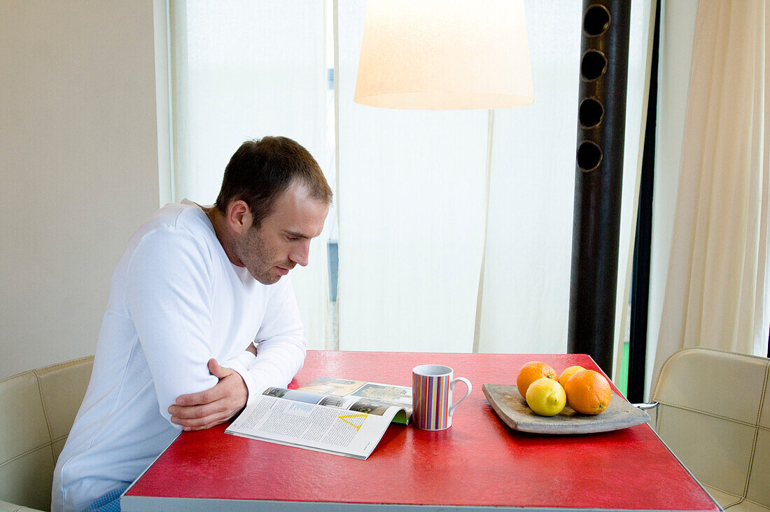 Man sitting in the kitchen, reading a magazine