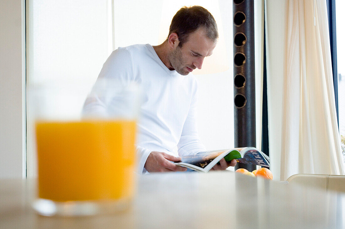 Man reading a magazine in the kitchen, orange juice in foreground