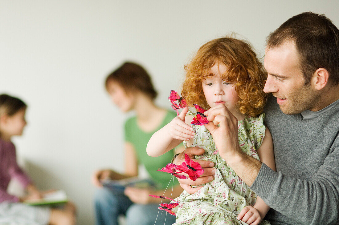 Man and little girl playing with butterfly garland, woman and child in the background