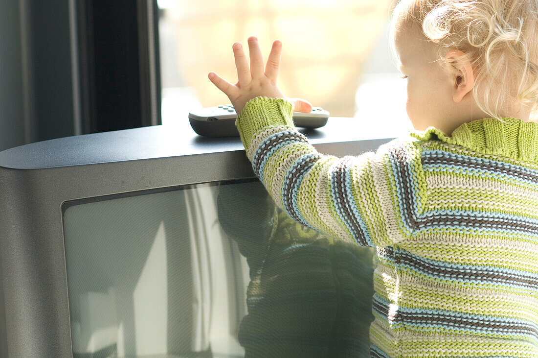 Little boy taking TV remote control, rear view