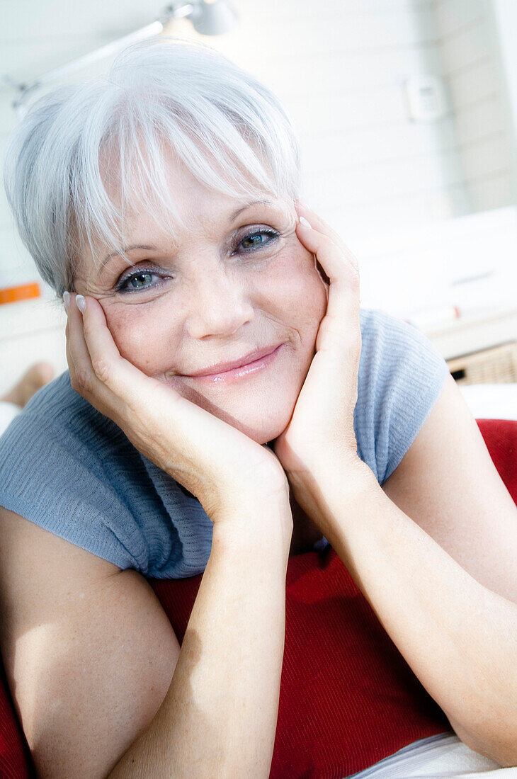 Senior woman lying on bed, looking at the camera