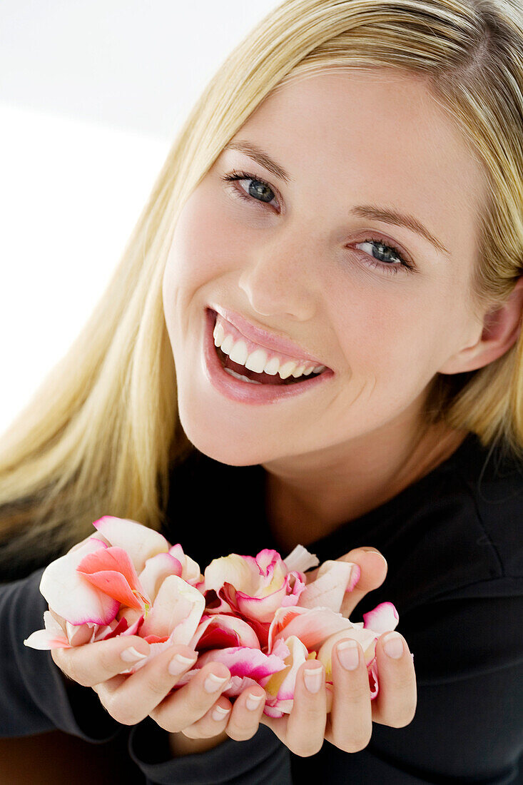 Portrait of a young woman smiling, holding flowers petals, indoors (studio)