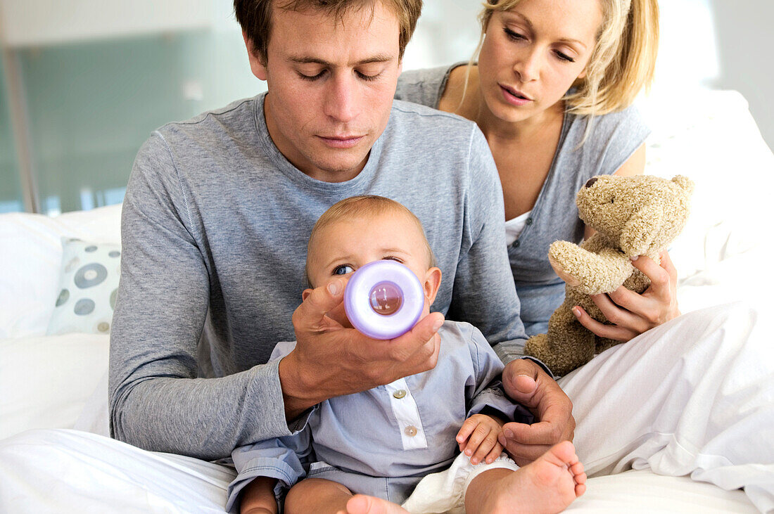 Young couple and baby sitting indoors, father feeding his son